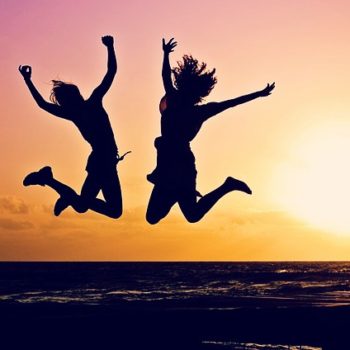 a silhouette of two girls jumping on the beach