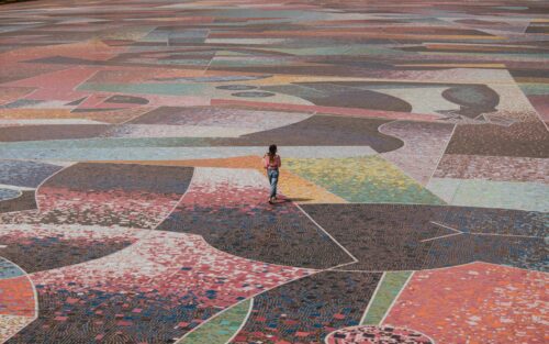Woman in pink blouse walking on a large and colorful mosaic