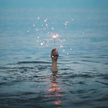 Hand emerging from water holding a sparkler.