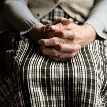 Hands of an elder joined together and resting on their lap.