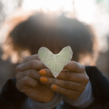 Woman extending her hands holding a heart-shaped leaf.