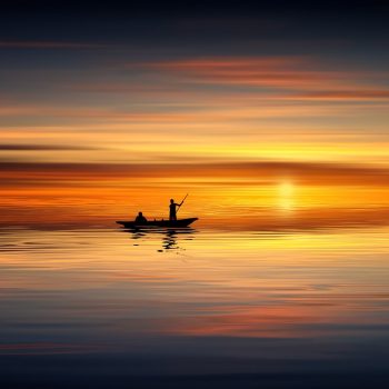 A person on a small boat in the water at sunset