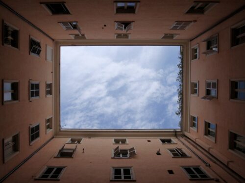View looking up at blue sky surrounded by four walls of an apartment building