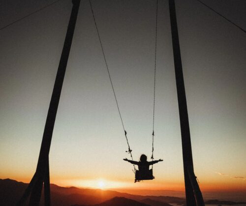 Silhouette of a child on a large swing at sunset