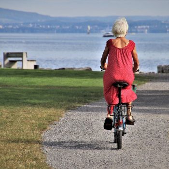 Elder riding a bicycle in a red dress.
