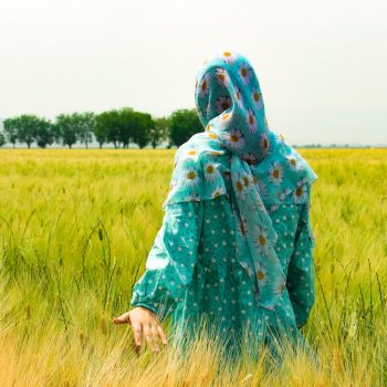 Woman walking through a field trailing her hand in the grass.