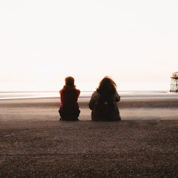 Two people sitting on a beach gazing at the sea.