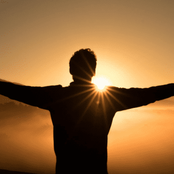 View from behind of silhouetted person standing in front of a golden sunrise.