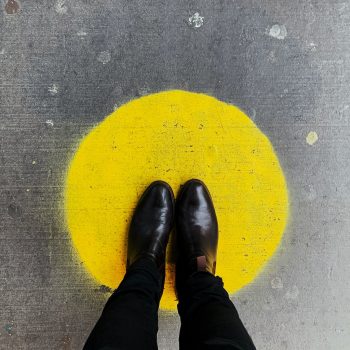A person in black pants and boots standing in a yellow spot painted on the ground