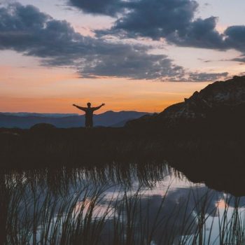 a person with their arms spread wide standing under a sunset