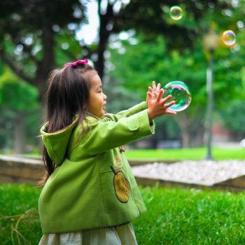 A young girl in a green jacket playing with bubbles