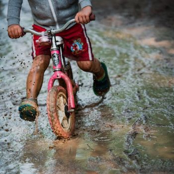 a child riding a pink bike through a puddle