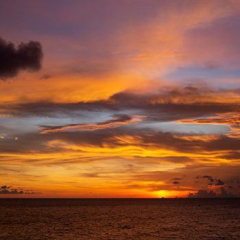 Sunset over the ocean with gold, orange, and purple clouds
