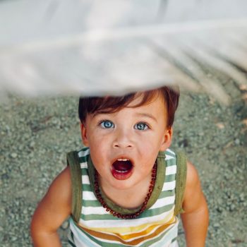 A young boy in a striped tank top looking up at a feather in awe