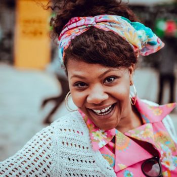 a photo of a woman smiling in a headband and white knit top