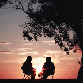 People sitting in chairs facing a sunset