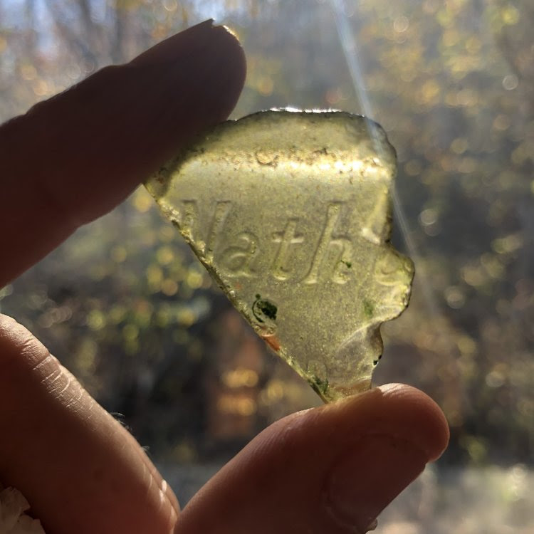 Hand holding up a piece of yellow sea glass to the light