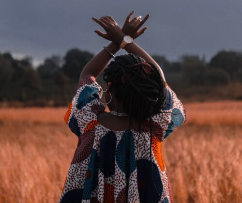 woman standing in a field with hands crossed over her head