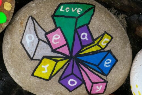 A rock painted with the words love, peace, and joy