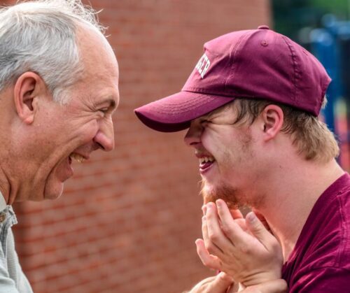 And older man smiling at a younger smiling man in a hat