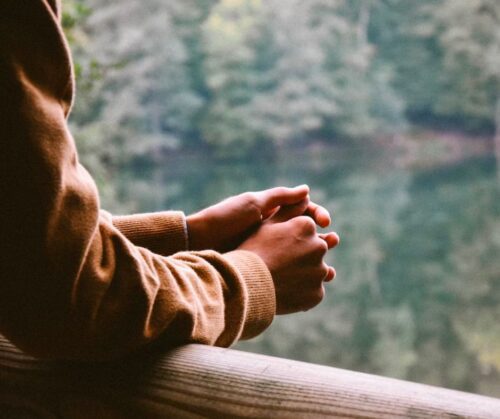 A person looking out over a body of water with their hands folded