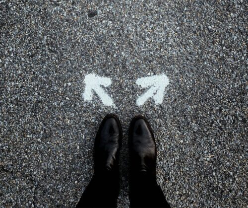 A person standing on asphalt with white arrows in front of their feet