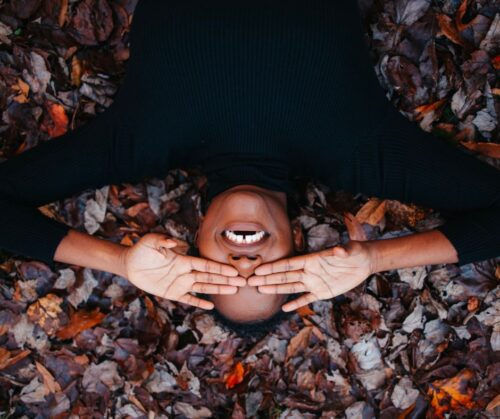 A women in a black shirt covering her eyes lying in dried leaves