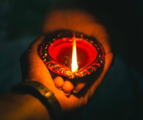 Close-up of a person's hands holding a lit candle. The flame of the candle is flickering slightly.