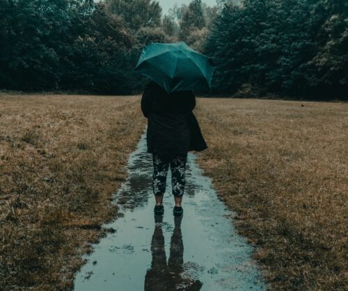 A woman walking away holding an umbrella - her reflection is visible in the wet walkway