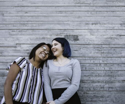 Two women laughing while standing in front of a wooden wall