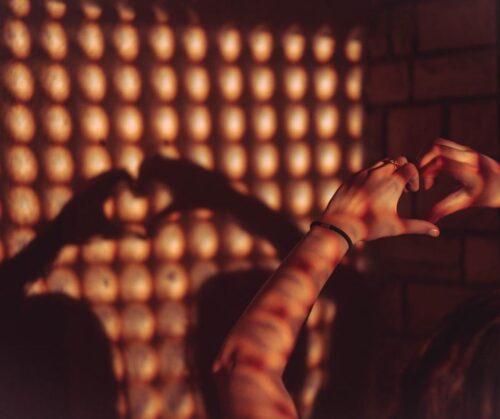 A person holding their hands in the shape of a heart casting a shadow on a wall