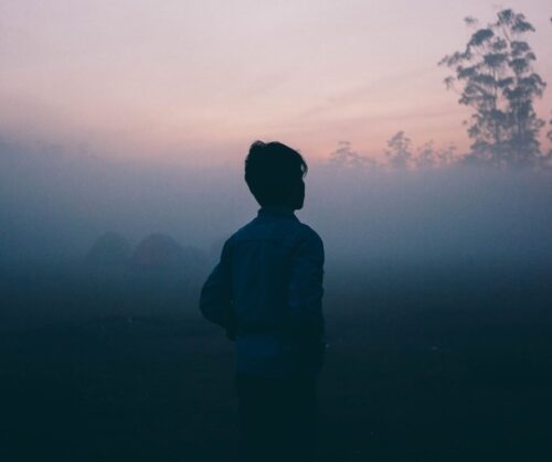 Silhouette of a person walking through hazy mist at dusk
