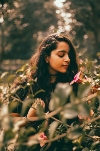 Young woman with her eyes closed smelling a pink flower