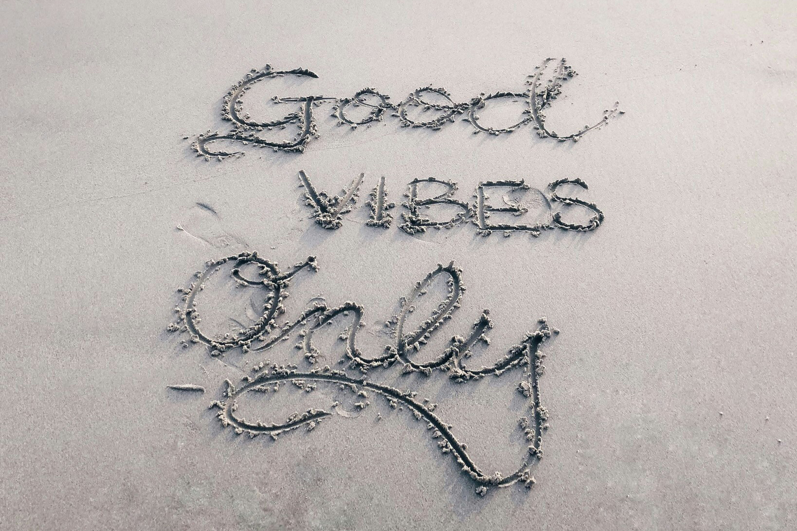 "Good vibes only" written in the sand at a beach
