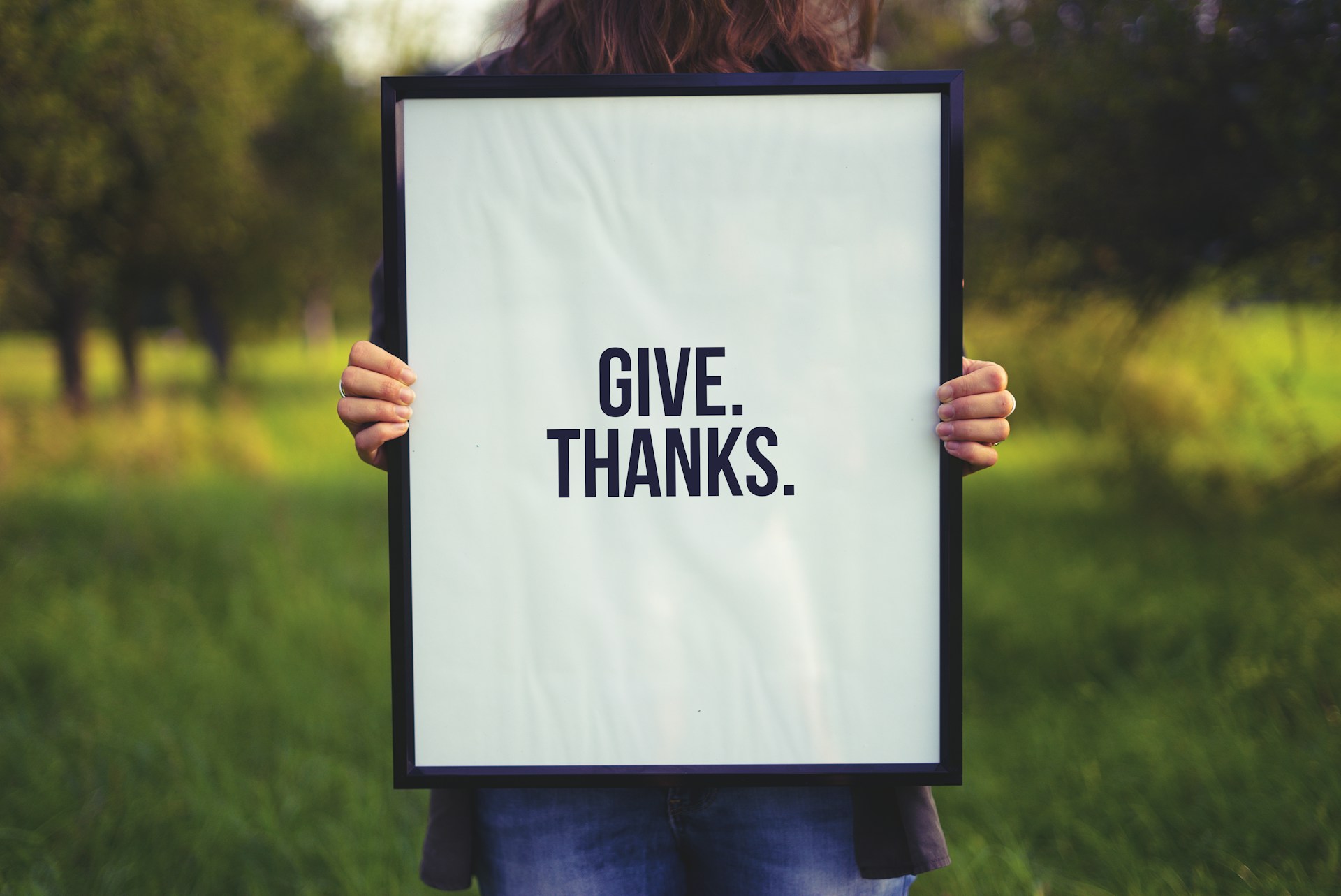 Person holding up a framed sign that says Give Thanks