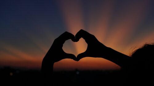 A person holding their hands in the shape of a heart with sunset as the backdrop