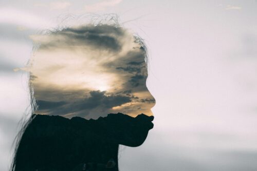 Silhouette of woman with sky superimposed over the silhouette of her face