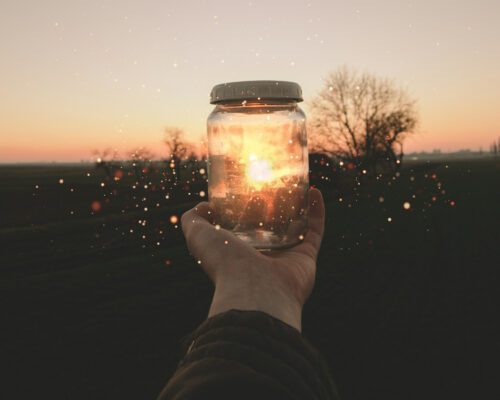 Person holding out a glass jar with glitter and light reflected