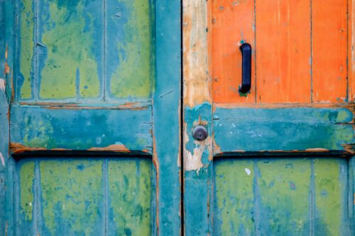 Closeup of panels of a colorful green, blue, and orange door with peeling paint