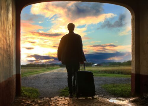 A man carrying luggage heading out onto an open road at sunset